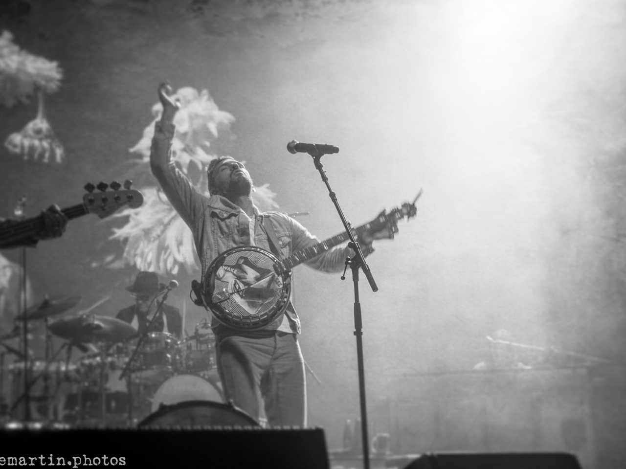 Black-and-white concert photo of Scott Avett on stage with a banjo, arm raised in the stage haze